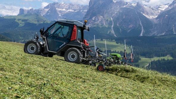 Fendt Twister The green Fendt Twister tedding hay in a mountain meadow with a blue sky and mountain in the background.